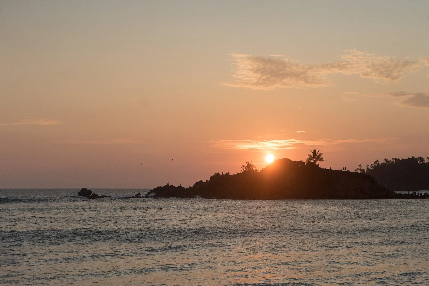 The sun setting behind Parrot Rock at Mirissa, with the sky glowing orange over the sea.