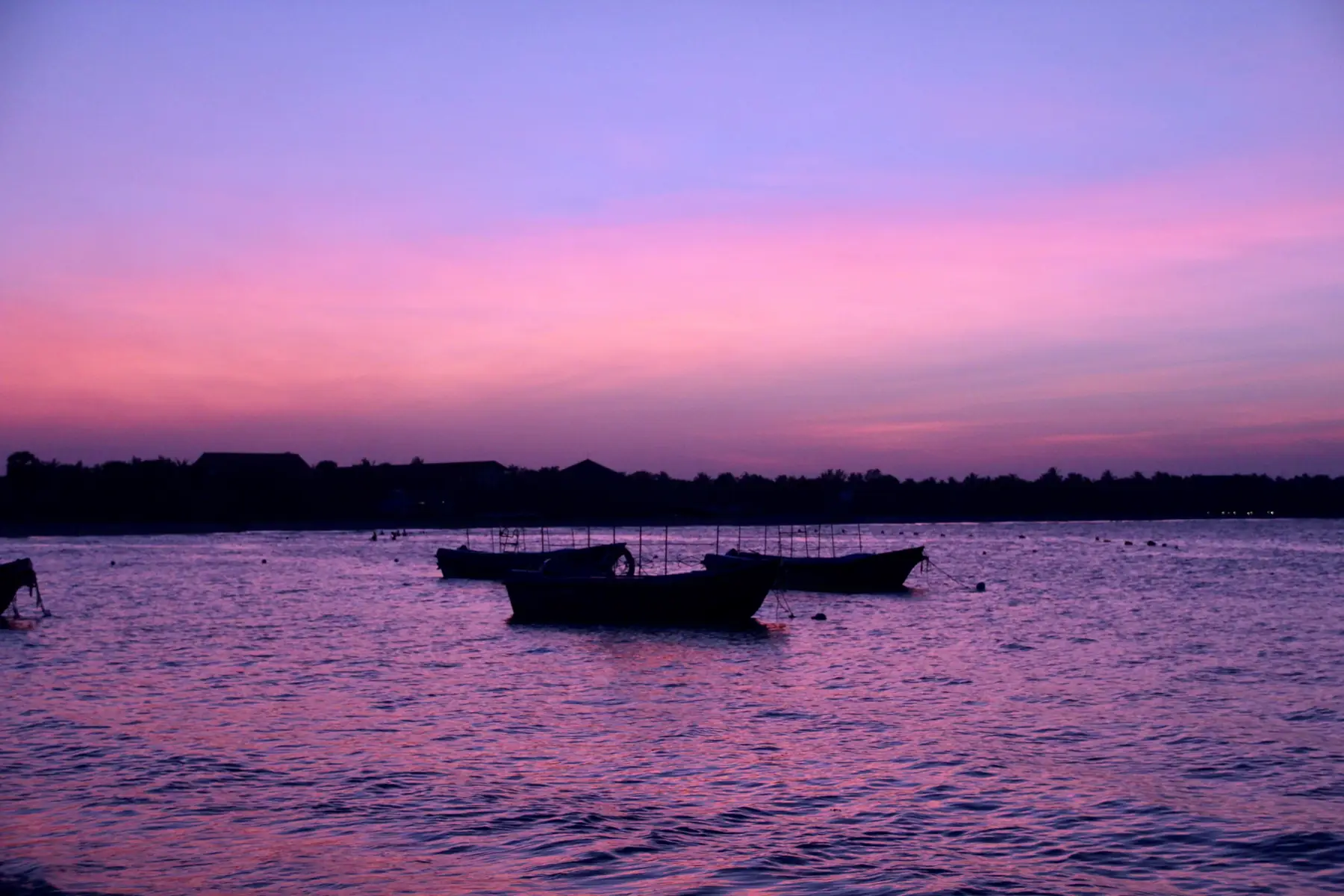 Small boats moored in the calm water of Pasikudah Bay under a pink evening sky.