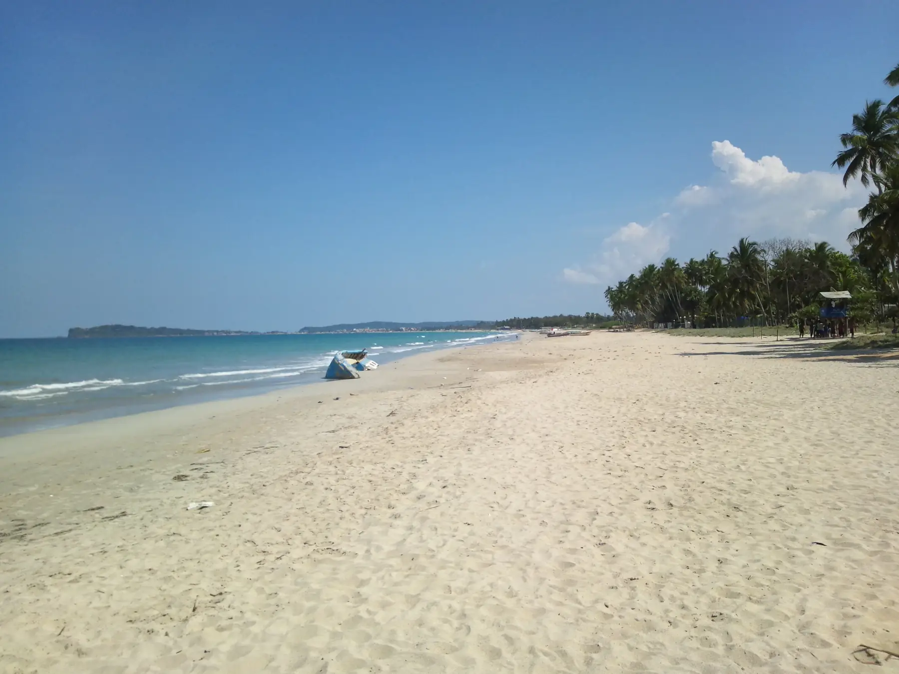 Wide white sand and calm blue water at Uppuveli Beach near Trincomalee, with palms on the right.