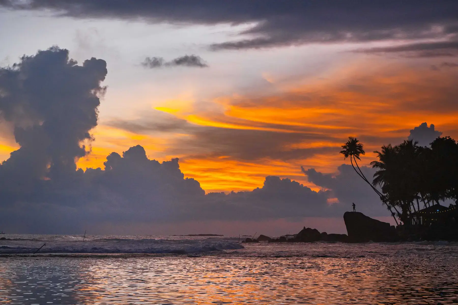 A dramatic orange and purple sunset over Unawatuna beach, palms in silhouette.