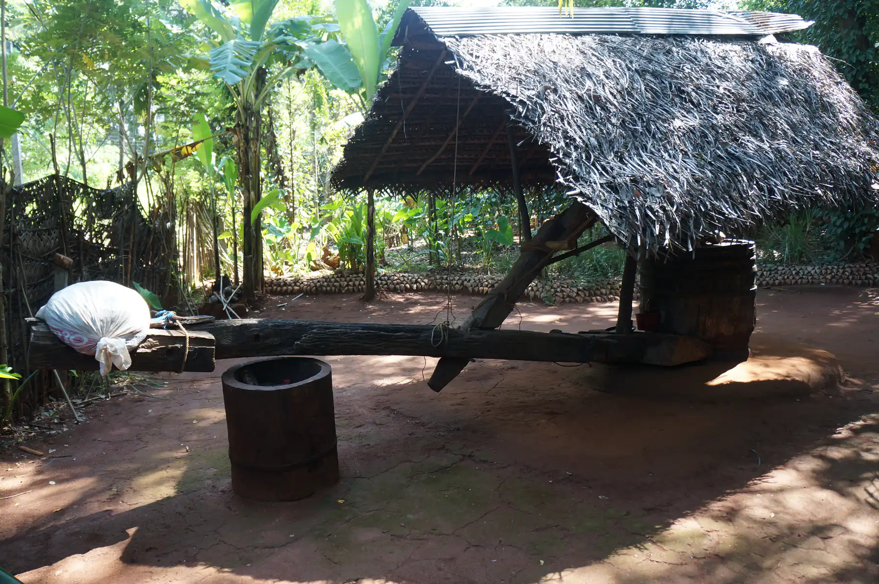A traditional wooden oil press under a thatched roof at a herbal garden in Matale, with no people or product labels in frame.
