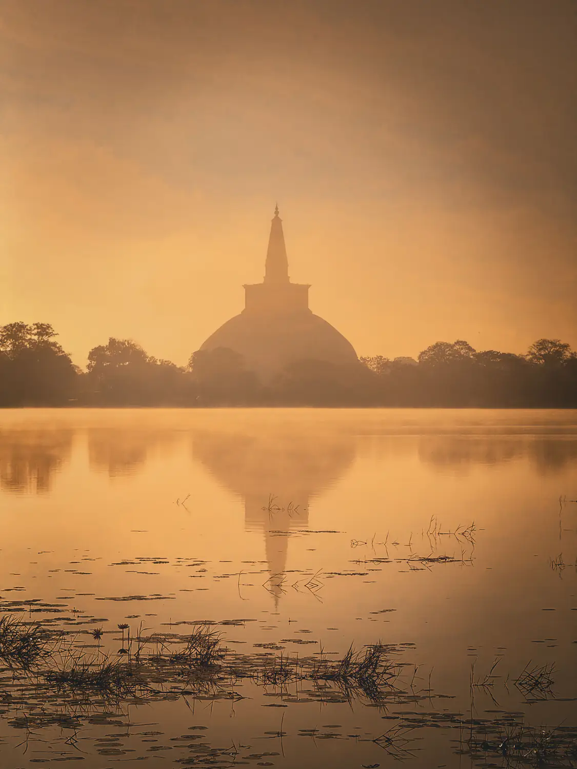 An Anuradhapura stupa silhouetted at sunrise and reflected in still water.