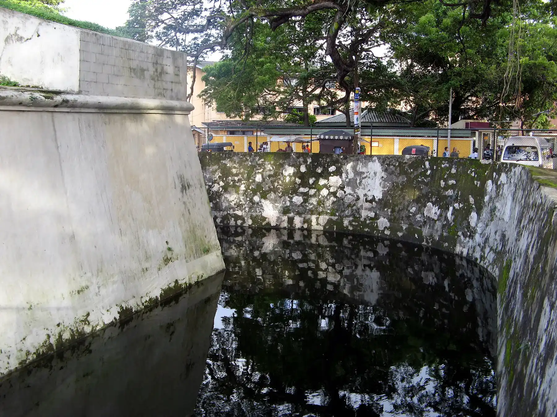 The thick white walls and stone-lined moat of the Dutch Star Fort in Matara, with trees and a yellow building behind.