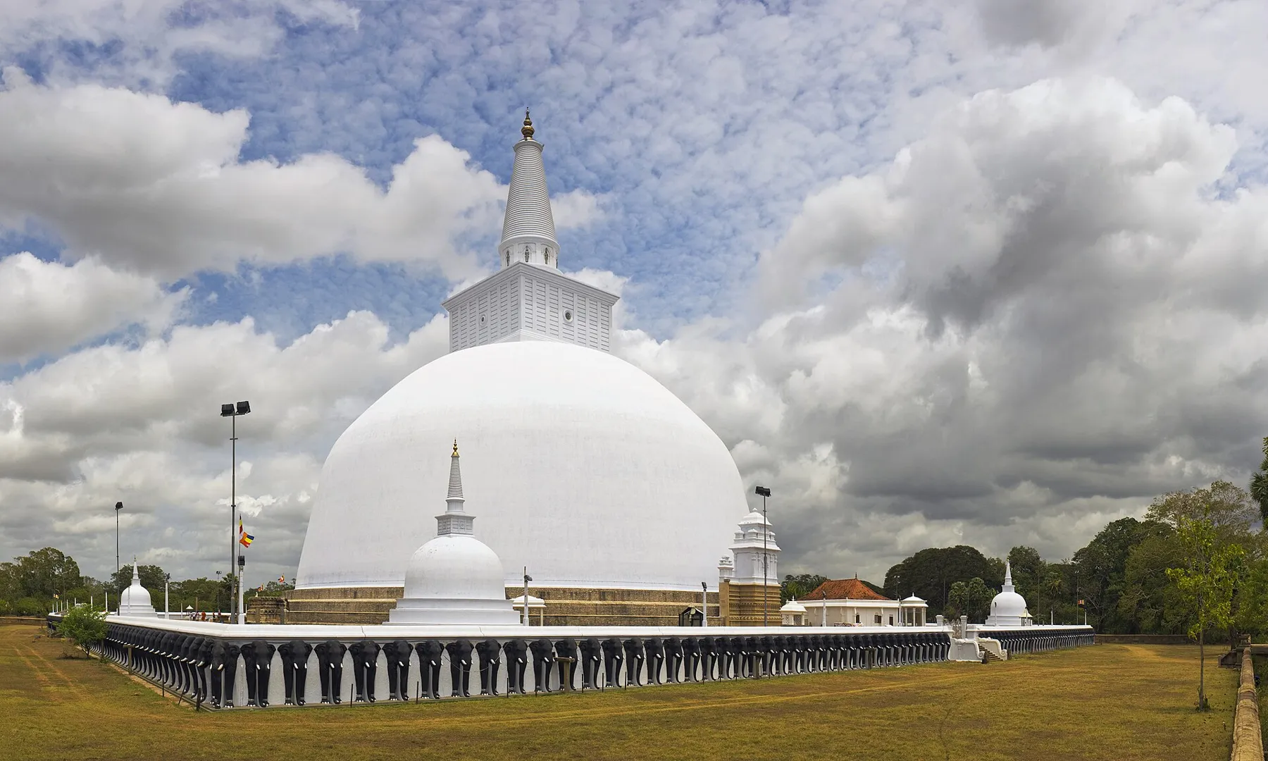 The great white dome of the Ruwanweli Saya stupa in Anuradhapura under a blue sky.